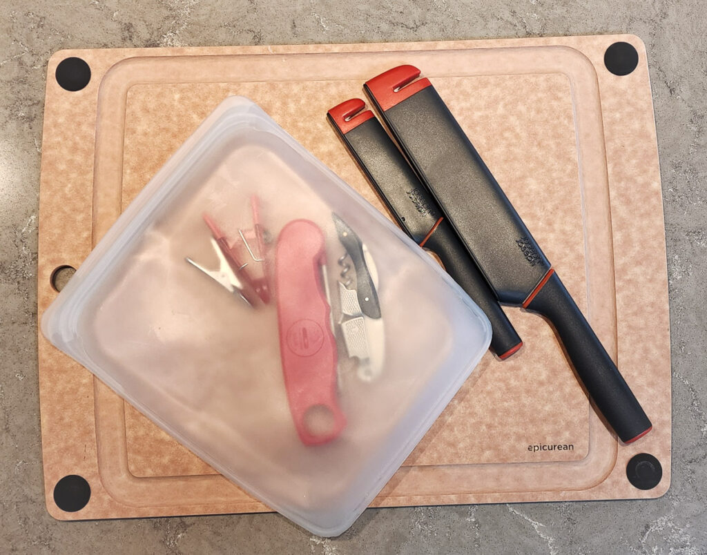a cutting board, knives, and bag of kitchen items displayed on a countertop