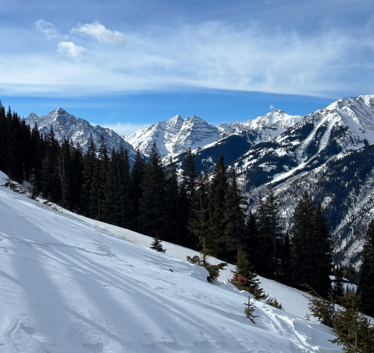 view of snowy peaks of the Maroon Bells from Aspen Highlands under a blue sky